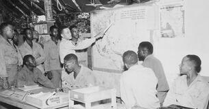 African American members of the 477th Antiaircraft Artillery study maps in an operations center.